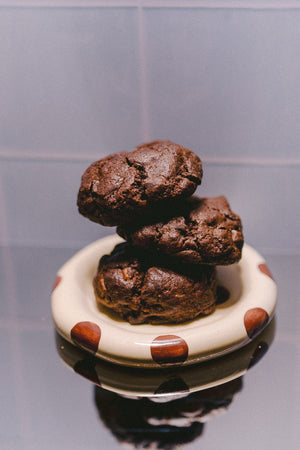 Milk it cookie dough bundle: stack of three baked dark chocolate cookies on a cream dish with brown spots