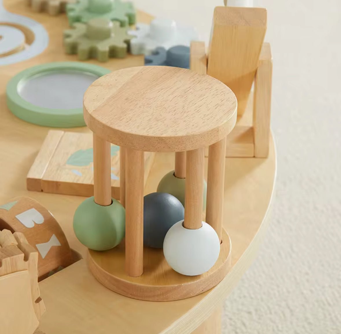 Wooden activity table, natural: close-up of the round wooden rattle drum with green, grey and white balls inside