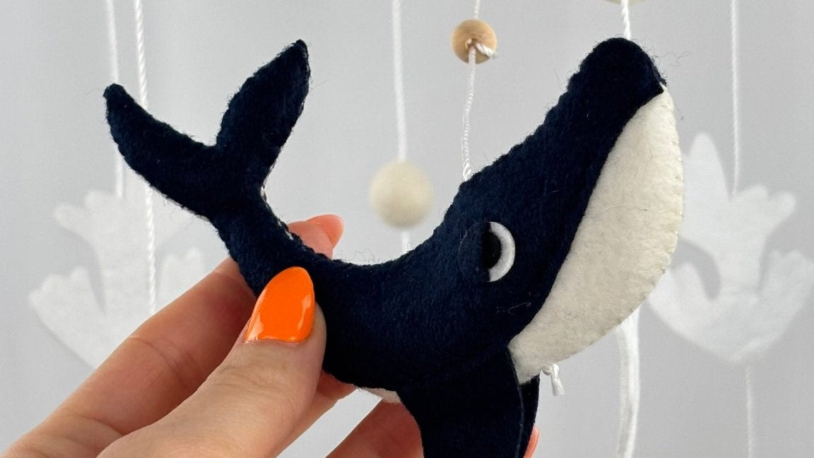 Ocean Whispers felt cot mobile detail of the navy and cream felt whale held in a hand
