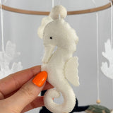 Ocean Whispers felt cot mobile detail of the cream felt seahorse with a wooden bead on its tail, held in a hand