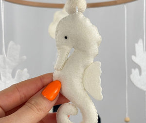 Ocean Whispers felt cot mobile detail of the cream felt seahorse with a wooden bead on its tail, held in a hand