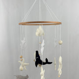 Ocean Whispers felt cot mobile hanging from a wooden hook, seen from a distance with whale, stingray and starfish