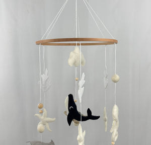 Ocean Whispers felt cot mobile hanging from a wooden hook, seen from a distance with whale, stingray and starfish