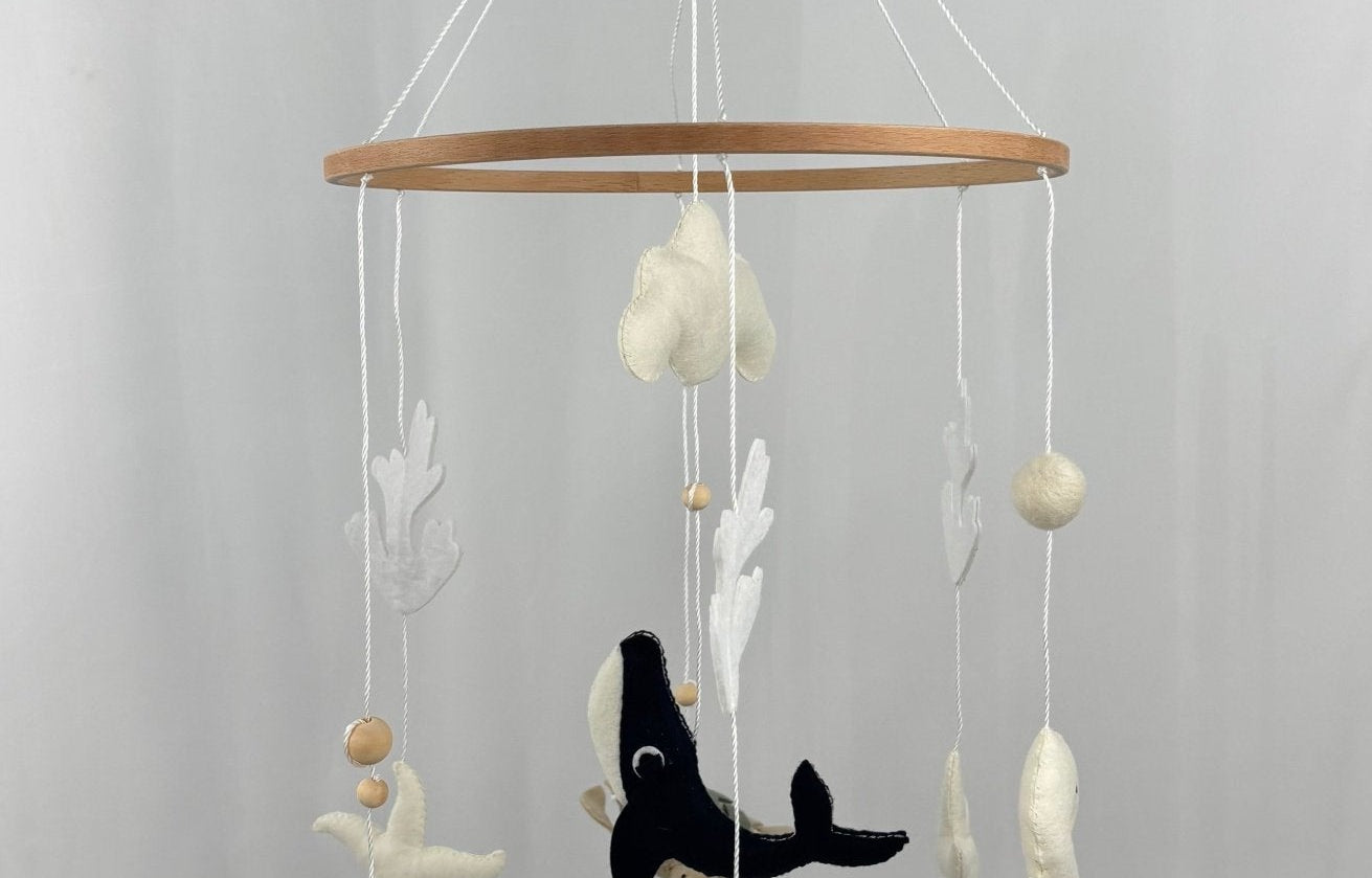 Ocean Whispers felt cot mobile hanging from a wooden hook, seen from a distance with whale, stingray and starfish