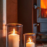 Palm Beach Hurricane Lanterns in two sizes holding lit pillar candles on a hearth beside a log burner