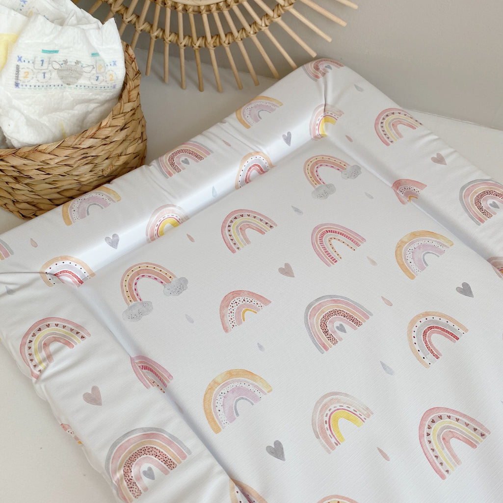 Standard Changing Mat Beau Rainbow Print on a surface beside a woven basket of nappies and a rattan sunburst mirror