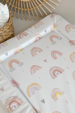 Standard Changing Mat Beau Rainbow Print on a surface beside a woven basket of nappies and a rattan sunburst mirror