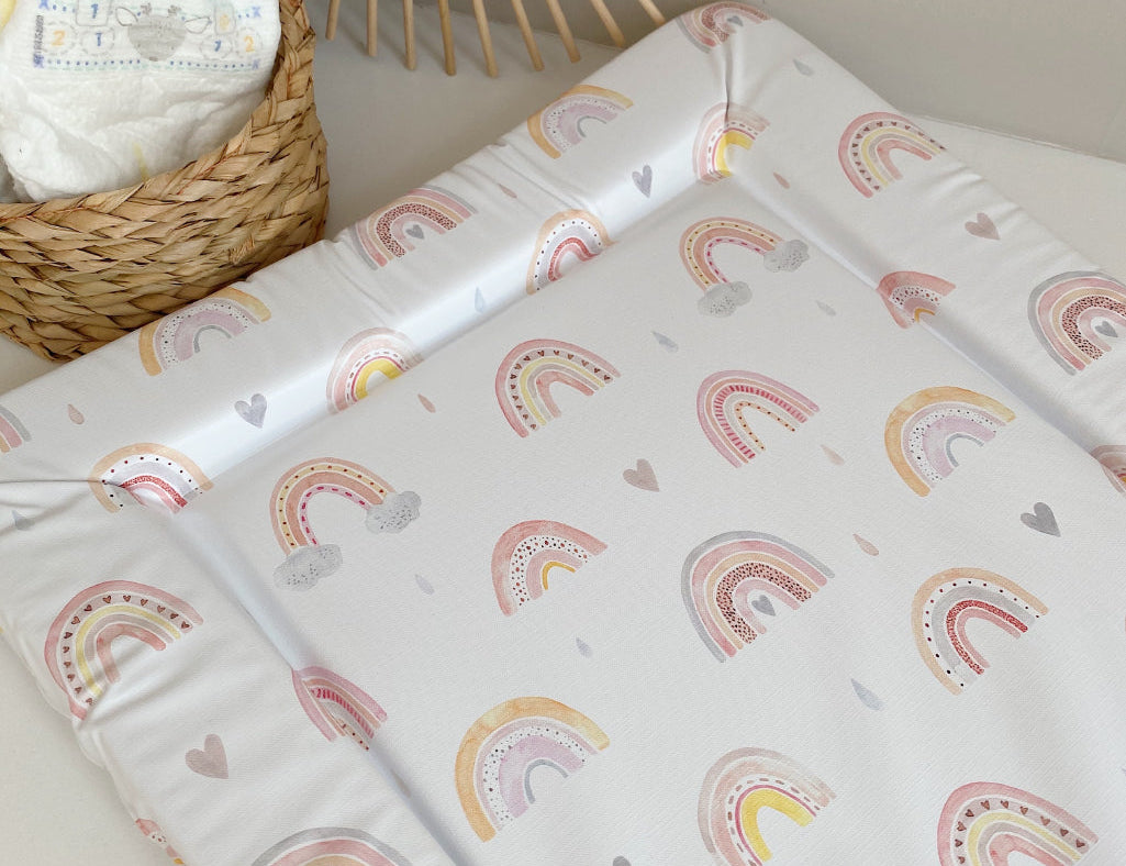 Standard Changing Mat Beau Rainbow Print on a surface beside a woven basket of nappies and a rattan sunburst mirror