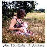 A woman in a colorful floral maternity dress breastfeeding a baby in a grassy outdoor field under a tree. The text 'Annie Breastfeeding in the Dali dress' is written at the bottom.