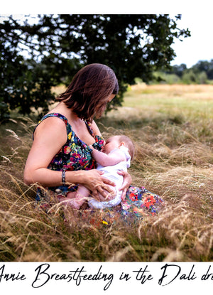 A woman in a colorful floral maternity dress breastfeeding a baby in a grassy outdoor field under a tree. The text 'Annie Breastfeeding in the Dali dress' is written at the bottom.