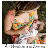 A woman in a colorful floral Dali dress breastfeeding a baby outdoors on grass. The photo has a white border with the text 'Lucy Breastfeeding in the Dali dress' at the bottom.