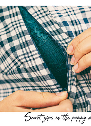 Close-up of a person's hands opening a dark teal zipper on a blue and white plaid garment, with the text 'Secret zips in the poppy dress' at the bottom.