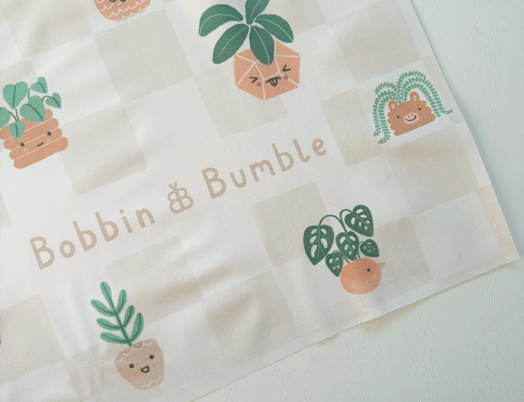 Splash Mat, Pot Plants: corner close-up showing the smiling plant pot print on a beige checkerboard background