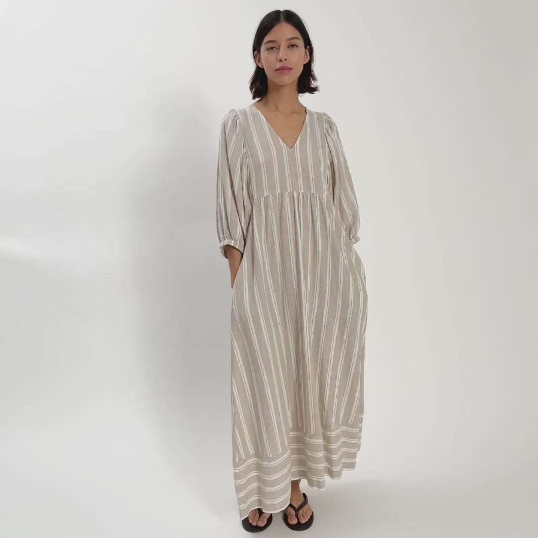 Woman wearing light coloured linen v neck dress moving around