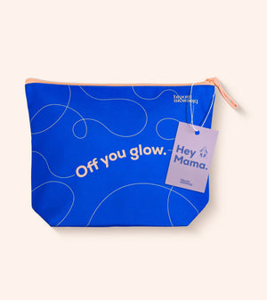A bright blue zippered pouch with white abstract line drawings and the text 'Off you glow.' on the front, featuring a lavender hangtag that reads 'Hey Mama.