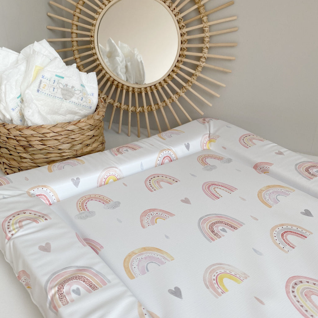 Standard Changing Mat Beau Rainbow Print at an angle, with nappies in a basket and a round rattan mirror behind