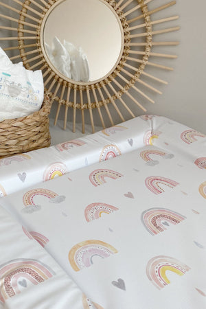 Standard Changing Mat Beau Rainbow Print at an angle, with nappies in a basket and a round rattan mirror behind