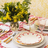 Rosy Red Scalloped Lunch Plate on a woven charger on a table with mimosa flowers, bamboo-handled cutlery and a pink glass