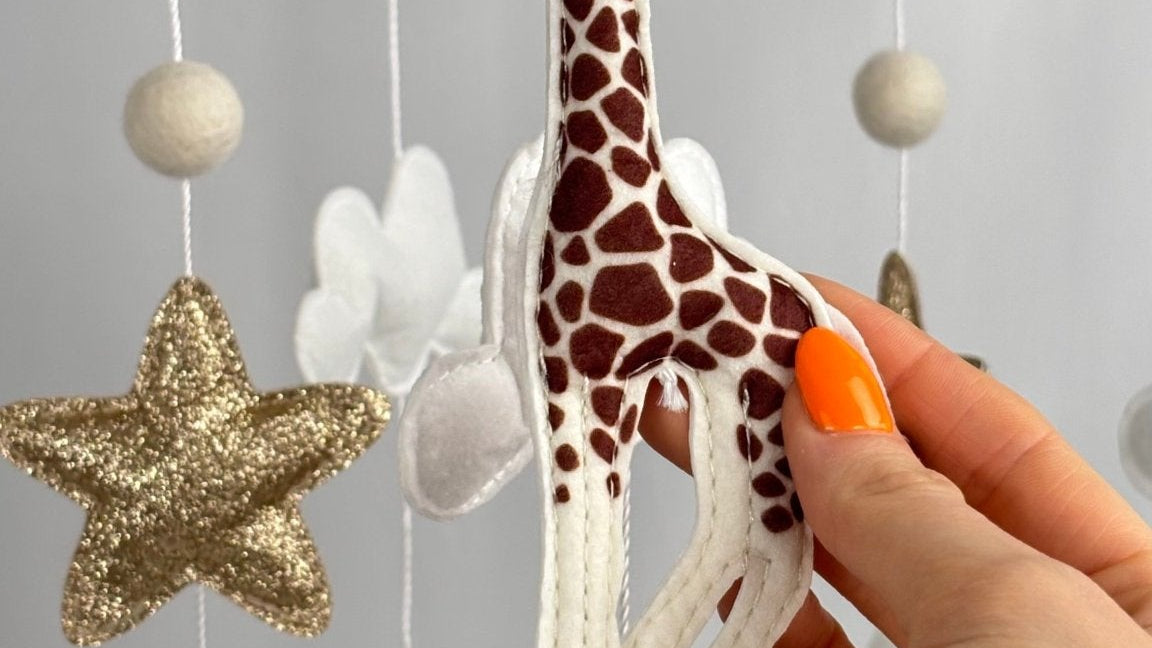 Safari Dreams Felt Cot Mobile with a hand holding the felt giraffe, showing its brown patches and stitched edges