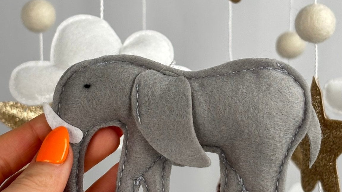Safari Dreams Felt Cot Mobile with a hand holding the grey felt elephant with a white tusk and stitched edges
