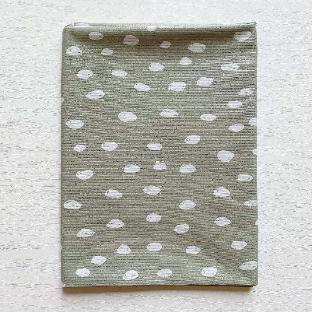 Splash Mat Sage Spots, folded flat on a white wooden surface showing the spotted pattern