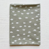 Splash Mat Sage Spots, folded flat on a white wooden surface showing the spotted pattern