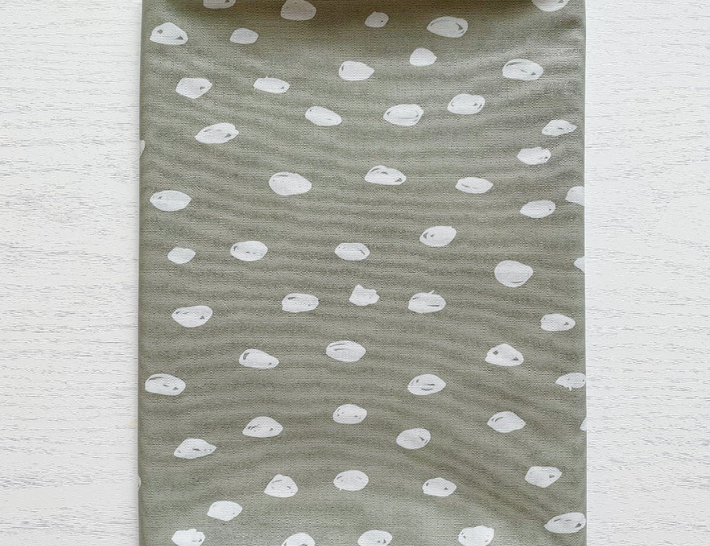 Splash Mat Sage Spots, folded flat on a white wooden surface showing the spotted pattern