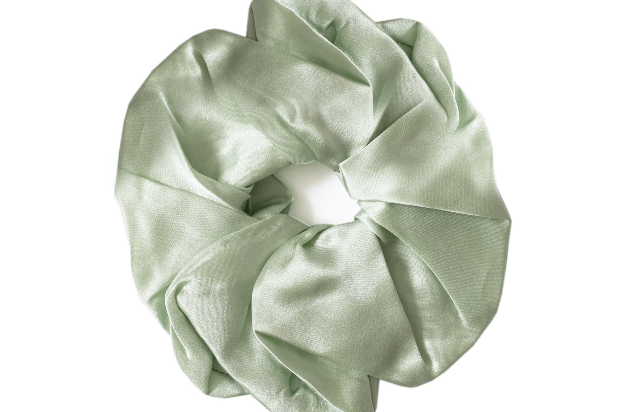 A sage green satin hair scrunchie with a gathered, pleated texture and a white elastic center band, shown on a plain white background.