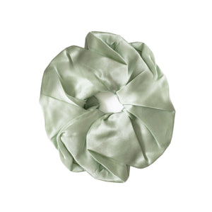 A sage green satin hair scrunchie with a gathered, pleated texture and a white elastic center band, shown on a plain white background.