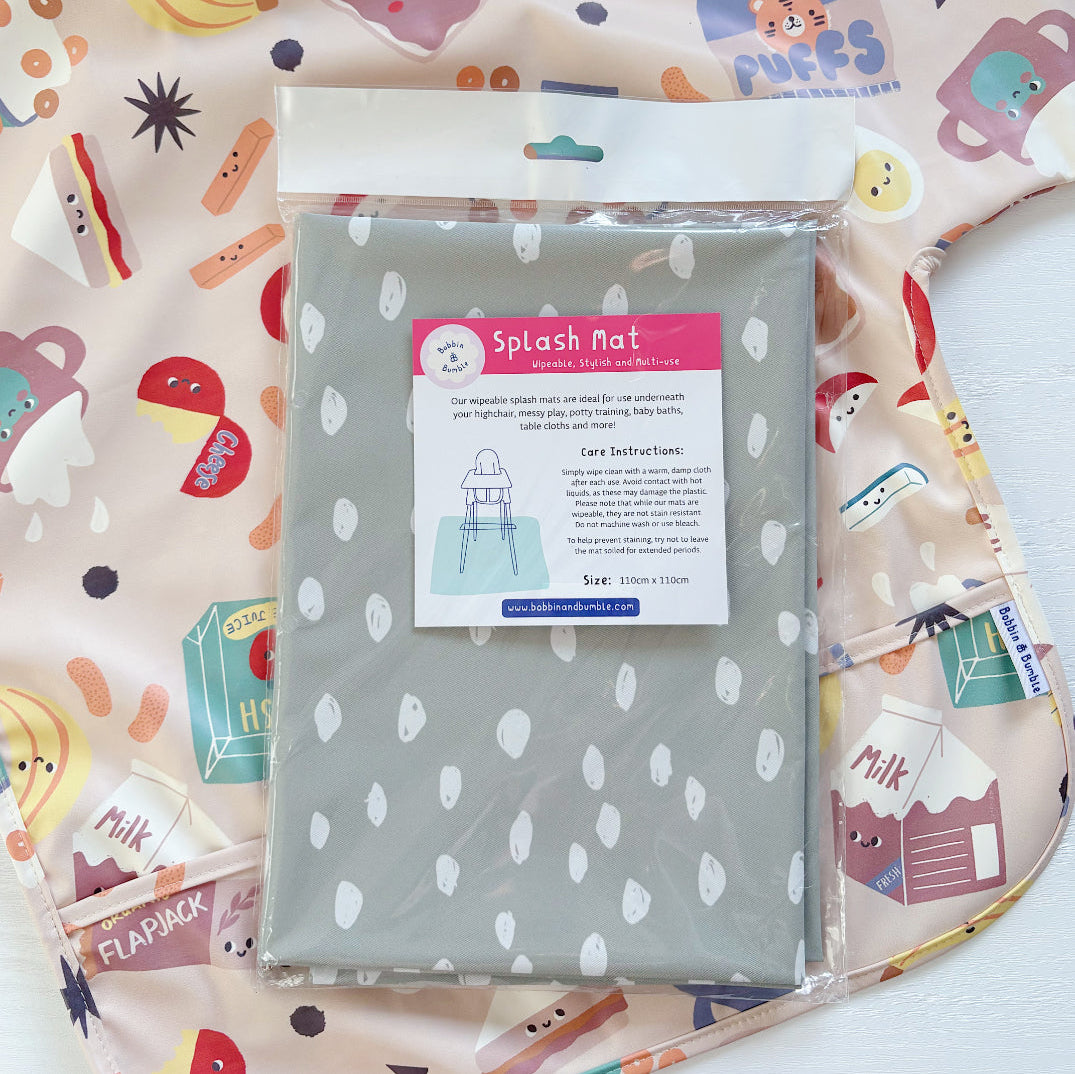 Splash Mat Sage Spots, in its packaging lying on a pink food-print sleeved bib