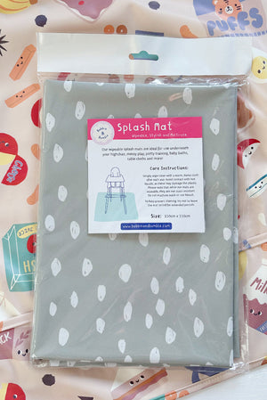 Splash Mat Sage Spots, in its packaging lying on a pink food-print sleeved bib