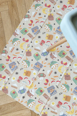 Splash Mat Snack Time seen from above on a herringbone wood floor, with highchair legs and tray edge at the side