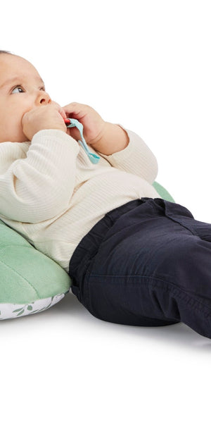 Sophie la girafe Cosy Play Cushion, baby reclining against the plain green quilted back of the cushion
