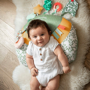 Sophie la girafe Cosy Play Cushion, seen from above with a smiling baby lying on it on a sheepskin rug