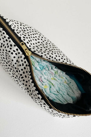 Nappy wallet in dalmatian print, zip partly open showing a black lining and a nappy tucked inside