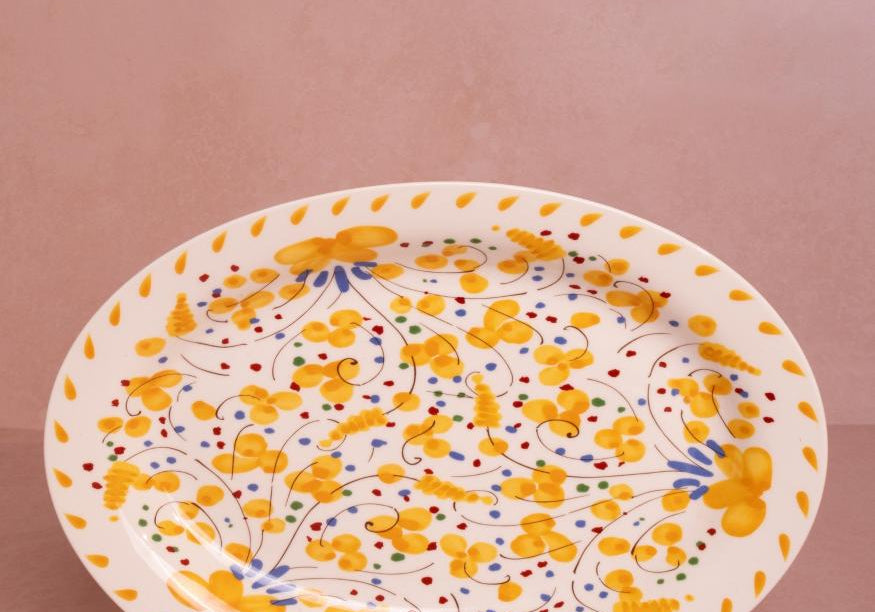 Sunshine Daisy Oval Serving Plate with a hand-painted yellow floral pattern and yellow petal border on a pink backdrop