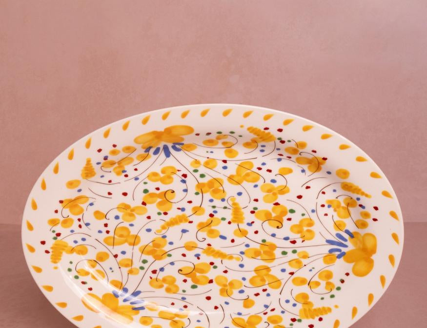 Sunshine Daisy Oval Serving Plate with a hand-painted yellow floral pattern and yellow petal border on a pink backdrop