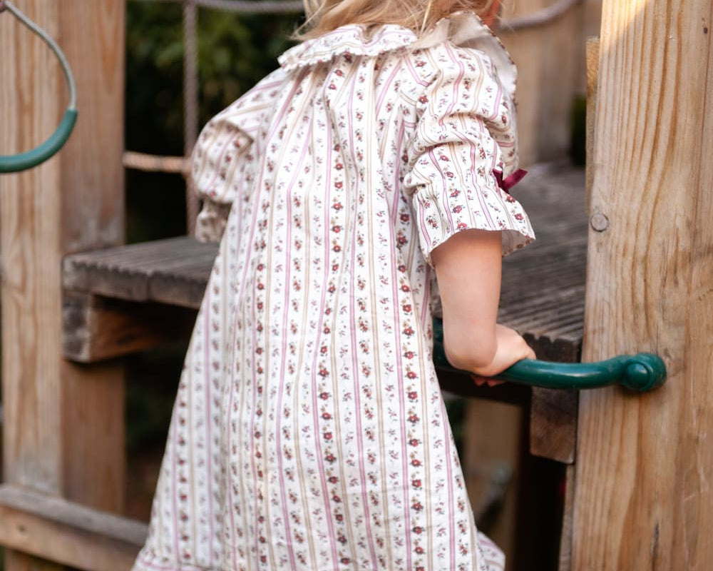Beatrice Rose Stripe nightie, back view of a child holding a green handle, showing the sleeve and frilled hem