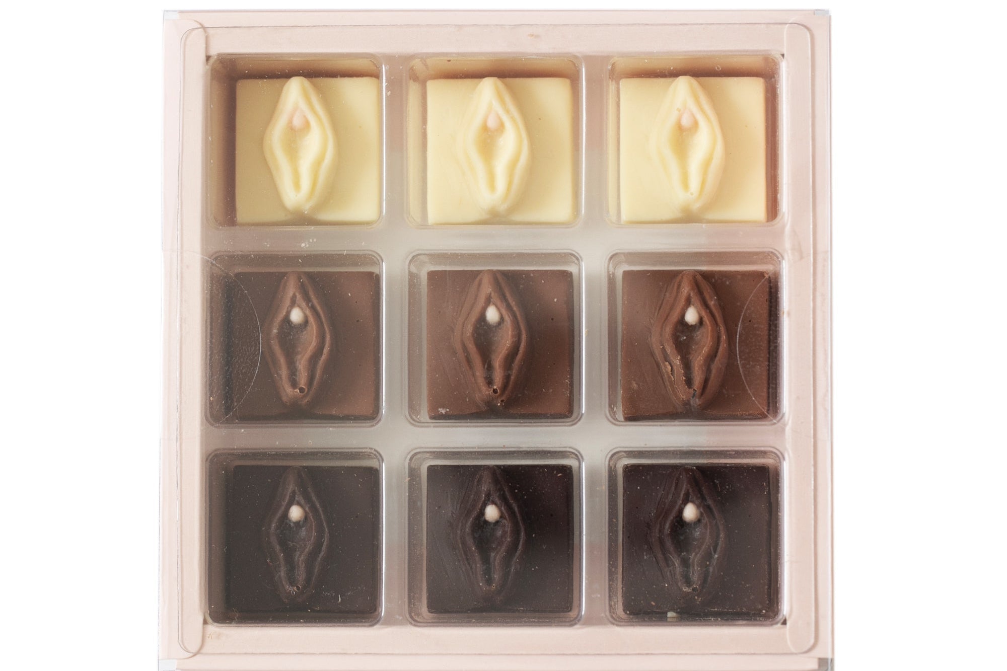 A 9-piece chocolate assortment in a clear plastic tray, featuring three milk chocolate pieces with a central heart and six dark chocolate pieces with a central eye, in cream and dark brown tones.