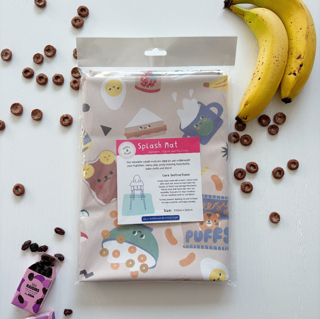 Splash Mat Snack Time folded in its clear packaging with a label, beside bananas and chocolate cereal rings