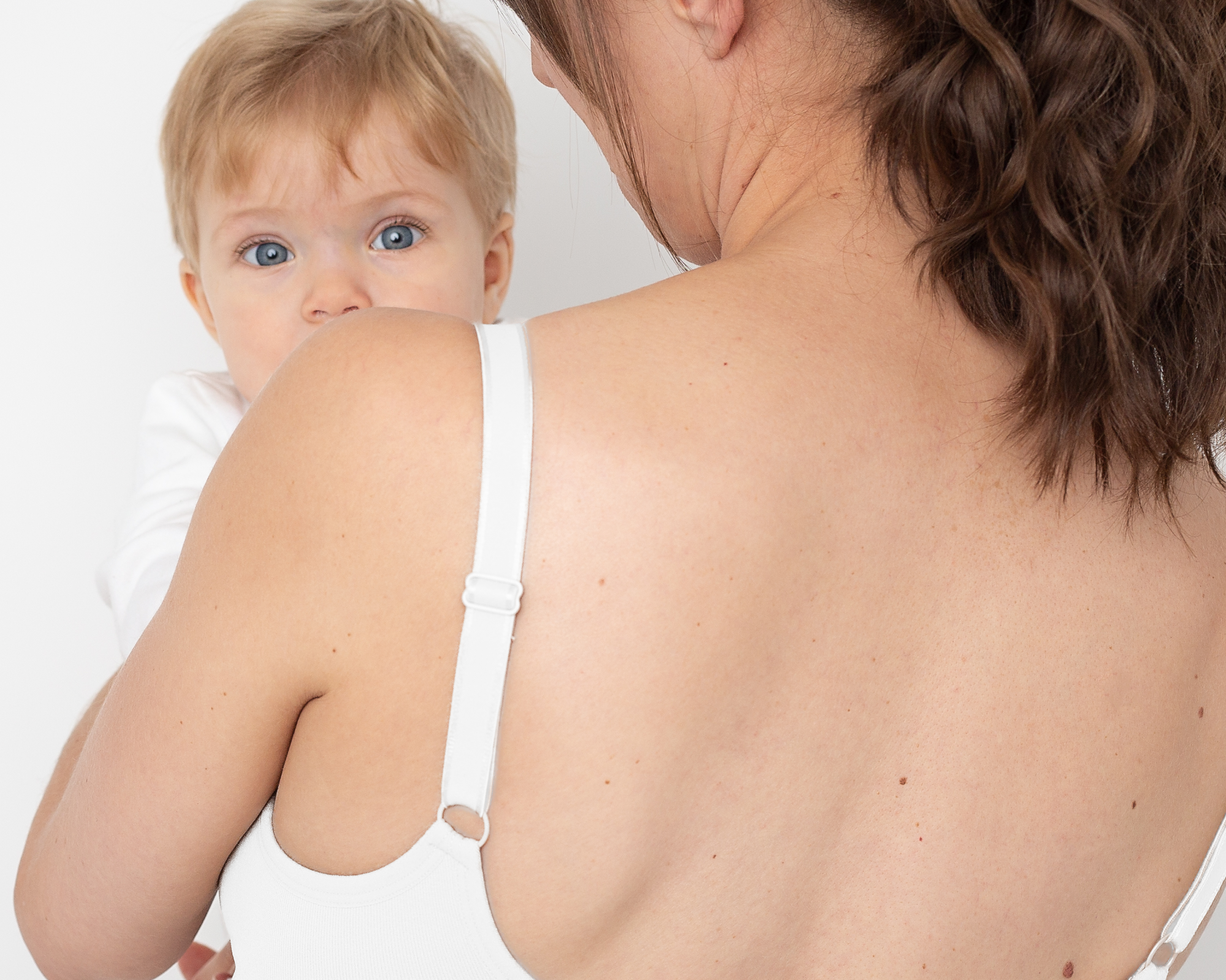 Woman wearing a white bra holding a baby against a white background