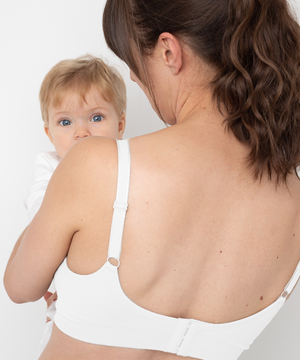 Woman wearing a white bra holding a baby against a white background