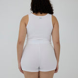 A person shown from the back wearing a white sleeveless tank top and matching white shorts against a plain light gray studio background.