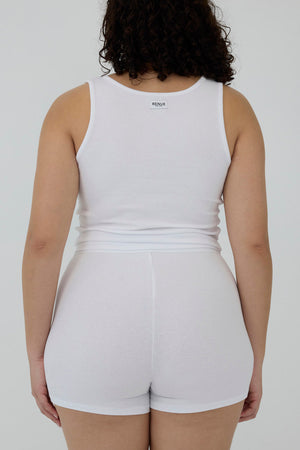 A person shown from the back wearing a white sleeveless tank top and matching white shorts against a plain light gray studio background.