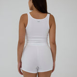 A woman shown from the back wearing a white sleeveless tank top and matching white shorts against a plain light gray studio background.