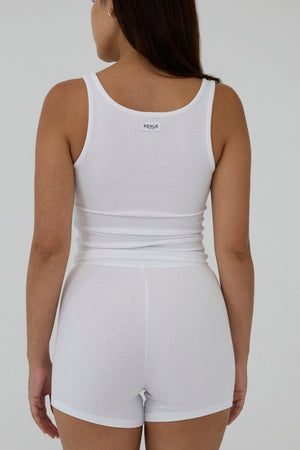 A woman shown from the back wearing a white sleeveless tank top and matching white shorts against a plain light gray studio background.