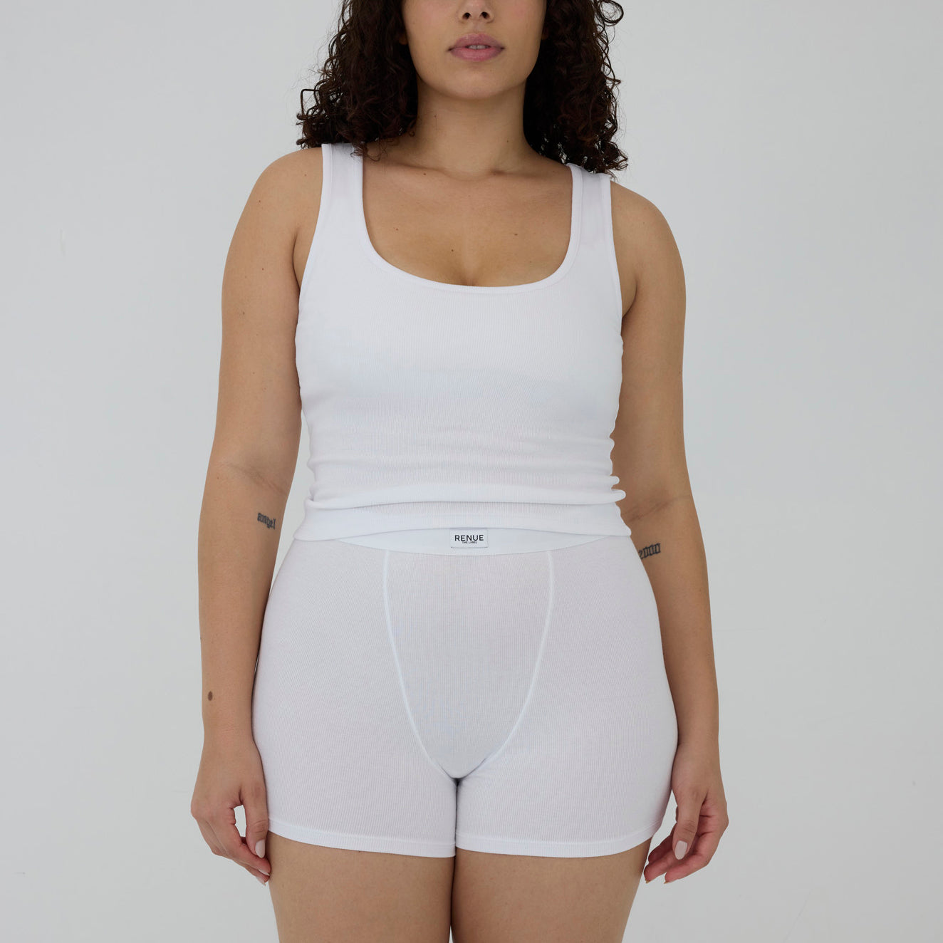 A model wearing a white ribbed tank top and matching white brief-style underwear shorts against a plain light gray studio background.