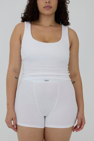 A model wearing a white ribbed tank top and matching white brief-style underwear shorts against a plain light gray studio background.